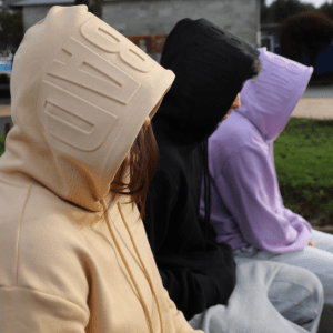 Models sitting side on wearing Due Hoodies in Tan, Black & Lavender